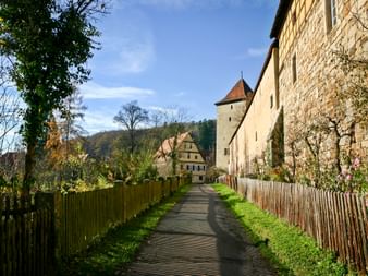 Historisches Kloster und Schloss Bebenhausen mit Steinmauern, Turm und Fachwerkhäusern entlang eines gepflasterten Weges in Tübingen.