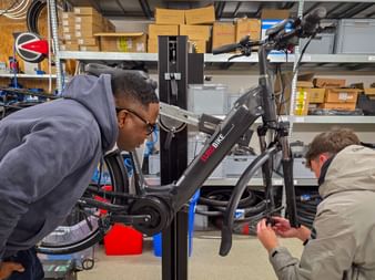 Two people examining an e-bike in a workshop during Eurofun Touristik Training Days 2026 in Mallorca, with storage shelves and boxes visible.