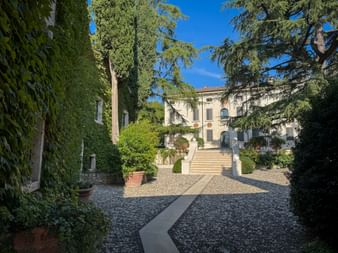 Villa Peverelli in Colognola ai Colli with stone staircase leading to entrance, surrounded by tall trees and manicured garden under blue sky.
