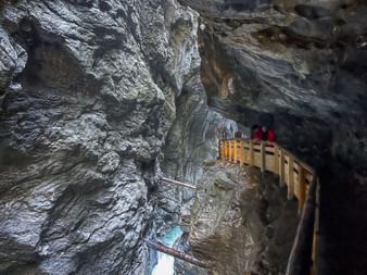 Wooden walkway with visitors in Liechtensteinklamm gorge, surrounded by dramatic gray rock walls with water flowing below.