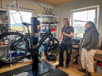 Three people in a bicycle workshop during Eurofun Touristik Training Days 2026. An e-bike is mounted on a repair stand while staff demonstrate maintenance.