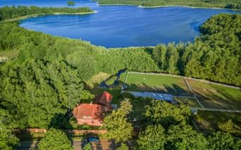 Luftaufnahme eines rot gedeckten Hauses umgeben von Wäldern nahe einem blauen See in der Masurischen Seenplatte, Polen.