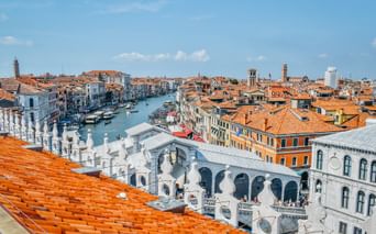 Panoramablick auf Venedigs Canal Grande mit der weißen Rialtobrücke, historischen Gebäuden mit Terrakottadächern und Booten auf dem Wasser.