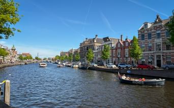 Der Fluss Spaarne in Haarlem mit traditionellen holländischen Häusern, am Kanal vertäuten Booten und einem vorbeifahrenden Ausflugsboot.