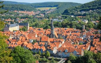 Panoramic view of Hann. Münden with red-tiled roofs, church towers, and half-timbered houses nestled in a green valley with forested hills.
