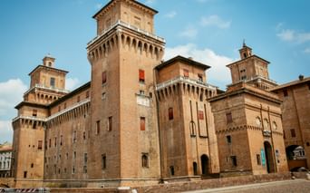 Castello Estense in Ferrara, eine mittelalterliche Backsteinburg mit hohen Türmen und Zinnen unter blauem Himmel mit weißen Wolken.