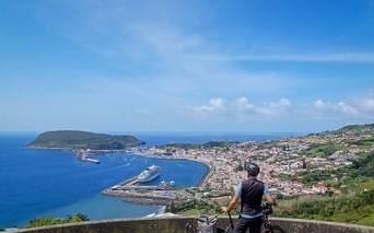 Radfahrer mit Fahrrad an Aussichtspunkt mit Blick auf Horta Hafen und Stadt auf den Azoren, mit Kreuzfahrtschiffen in der Bucht.
