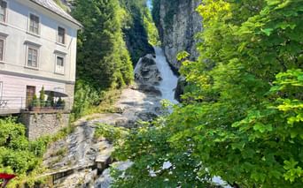 Waterfall cascading through rocky gorge in Bad Gastein, framed by green trees and a white building on the left.