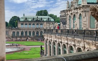 Blick auf den barocken Innenhof des Dresdner Zwingers mit verzierten Sandsteingebäuden, grünen Kupferdächern, Skulpturen und Rasen.