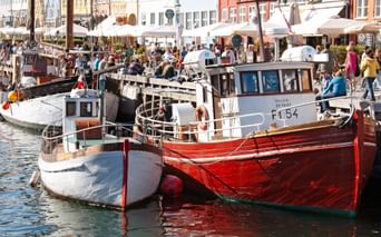 Traditional fishing boats moored in Nyhavn harbor, Copenhagen. Colorful historic buildings and outdoor cafes line the waterfront with visitors.