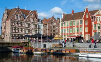 Bunte flämische Giebelhäuser entlang des Graslei-Kanals in Gent mit Booten am Ufer und Menschen auf dem Kai.