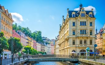 Historic Karlsbad old town with colorful buildings along the Tepla River. A yellow baroque building with blue roof stands prominently by the bridge.