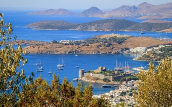Luftaufnahme der Burg Bodrum und des Hafens mit Segelbooten im Golf von Gökova. Berge und Inseln in der Ferne unter blauem Himmel.