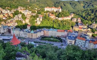 Aerial view of Karlsbad spa town with colorful historic buildings along a central square, surrounded by forested hills and green valleys.