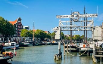 Hafen Wolwevershaven in Dordrecht mit historischen Booten, Industriekran mit L. Straatman-Schild, bunten Häusern und Kirchturm unter blauem Himmel.