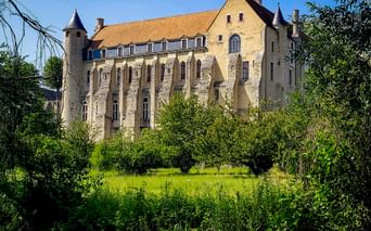Historic Abbaye Saint-Séverin in Château-Landon with stone walls, arched windows, and round towers, surrounded by green meadow and trees.