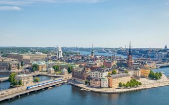 Panoramic view of Riga's historic Old Town on an island surrounded by water, with church spires, colorful buildings, and bridges under blue sky.