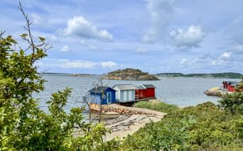 Colorful boathouses in blue, white and red on rocky shore at Brottkärs, Sweden. Calm water with small islands under cloudy sky.