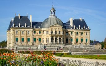 Château de Vaux-le-Vicomte with its distinctive dome and classical French architecture, surrounded by formal gardens with colorful flowers.