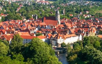 Aerial view of Hann. Münden old town with red-tiled roofs, church spires, and a river flowing through green landscape.