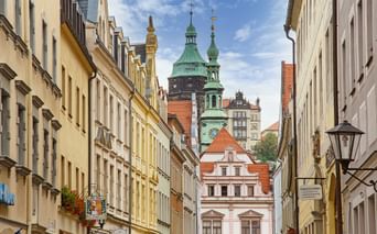 Narrow street in Pirna with colorful historic buildings leading to a church with green copper spires under blue sky.