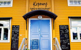 Ein Cafe in einem gelben landestypischen Holzhaus mit blauer Eingangstür