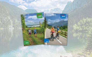 Zwei Eurohike-Kataloge 2025 vor Bergsee-Kulisse. Links Wanderkatalog mit Wanderern, rechts Radkatalog mit Radfahrern.