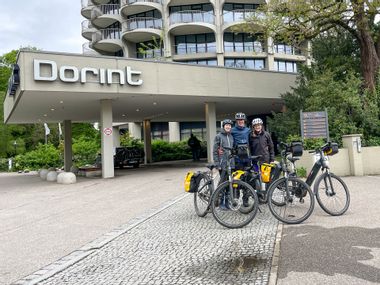 Three cyclists with e-bikes in front of hotel
