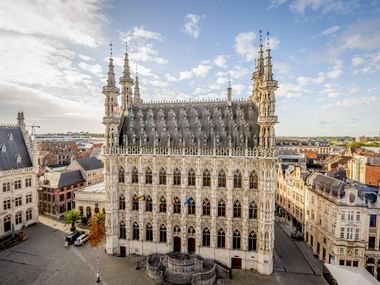 Ornate Gothic Town Hall of Leuven with elaborate stone facade, spires, and statues. The building overlooks a square surrounded by historic buildings.