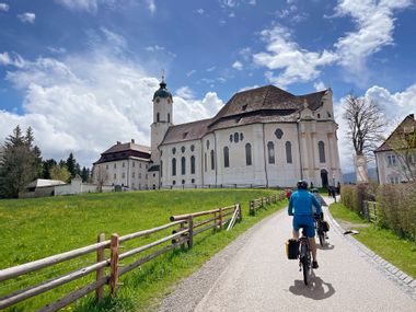 Radfahrer fahren auf Weg an Wieskirche vorbei