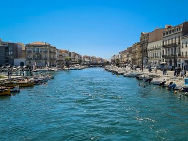 Blauer Kanal in Sète mit Fischerbooten an beiden Seiten, gesäumt von historischen Gebäuden unter klarem Himmel in Südfrankreich.