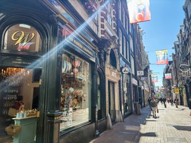 Einkaufsstraße Heiligeweg in Amsterdam mit historischen Gebäuden, Geschäften und Fußgängern. Bunte Banner hängen über der Kopfsteinpflasterstraße.