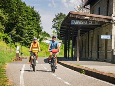 A woman and a man cycle past the abandoned Tarvisio Citta railway station