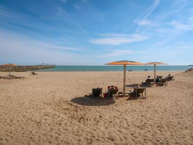 Sandy beach in Saint-Nazaire with orange parasols and deck chairs. People relax under umbrellas with calm sea and blue sky in background.
