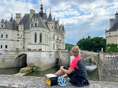 Eine Radfahrerin sitzt auf einer Steinmauer vor dem Schloss Chenonceau an der Loire