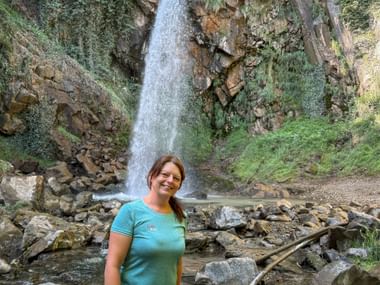 Woman in turquoise shirt standing before a waterfall cascading over moss-covered rocks on the Brandis Waalweg near Meran.