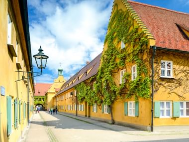 Gelbe Gebäude mit efeubedeckten Wänden und roten Ziegeldächern säumen die Herrengasse in Augsburgs historischer Fuggerei.