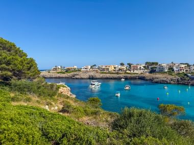 Türkisfarbene Bucht Cala Marcal bei Porto Colom mit Booten im ruhigen Wasser, umgeben von felsiger Küste und mediterraner Vegetation.