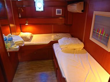 Kompakte Kabine auf MS Lestello mit zwei Einzelbetten, Holzverkleidung, Klimaanlage, Fenster und buntem Wandbild.