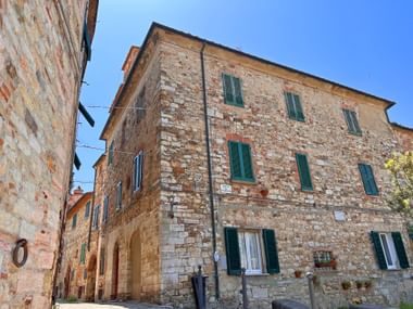 Narrow street in Suvereto with weathered stone buildings featuring green shutters under a clear blue sky in Tuscany.