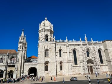Hieronymus-Kloster in Lissabon mit verzierter manuelinischer Architektur, Glockenturm und dekorativer Fassade unter blauem Himmel.