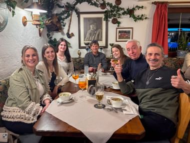 Seven people seated at a restaurant table with drinks and soup bowls, smiling at the camera in a traditional decorated dining room.