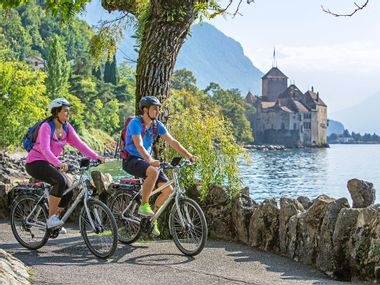 Two cyclists on the lakeside cycle path in front of Chillon Castle