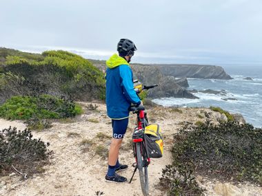 Radfahrer neben Fahrrad mit Küste und Meer im Hintergrund