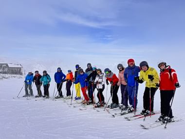 Large group of skiers in colorful winter clothing posing together on snowy slopes in Obertauern with mountain buildings in background.