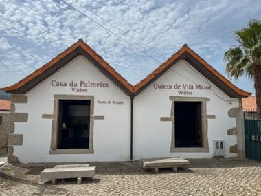 White building with orange tile roof and two entrances labeled Casa da Palmeira and Quinta de Vila Maior, both wine sales points in Douro.