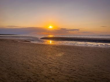 Sandstrand in Caorle bei Sonnenuntergang mit ruhigen Wellen und goldenem Licht auf dem nassen Sand und der Adria.