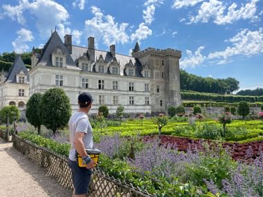 Cyclist with helmet viewing a French Renaissance castle along the Loire cycle route. Ornamental gardens with colorful flowers in foreground.