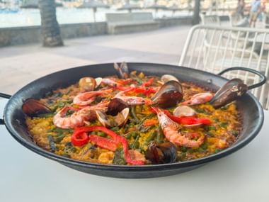 Traditionelle Paellapfanne mit Garnelen, Muscheln und Paprika auf Safranreis, serviert in einem Hafenrestaurant in Port de Sóller.