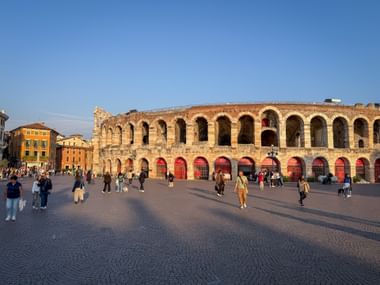 Ancient Roman amphitheater Arena di Verona with characteristic arches and red gates. Tourists walk across the cobblestone square in front.